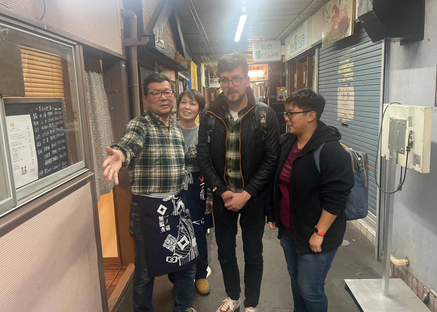 A chef greeting a small group at the entrance of a yokocho alley