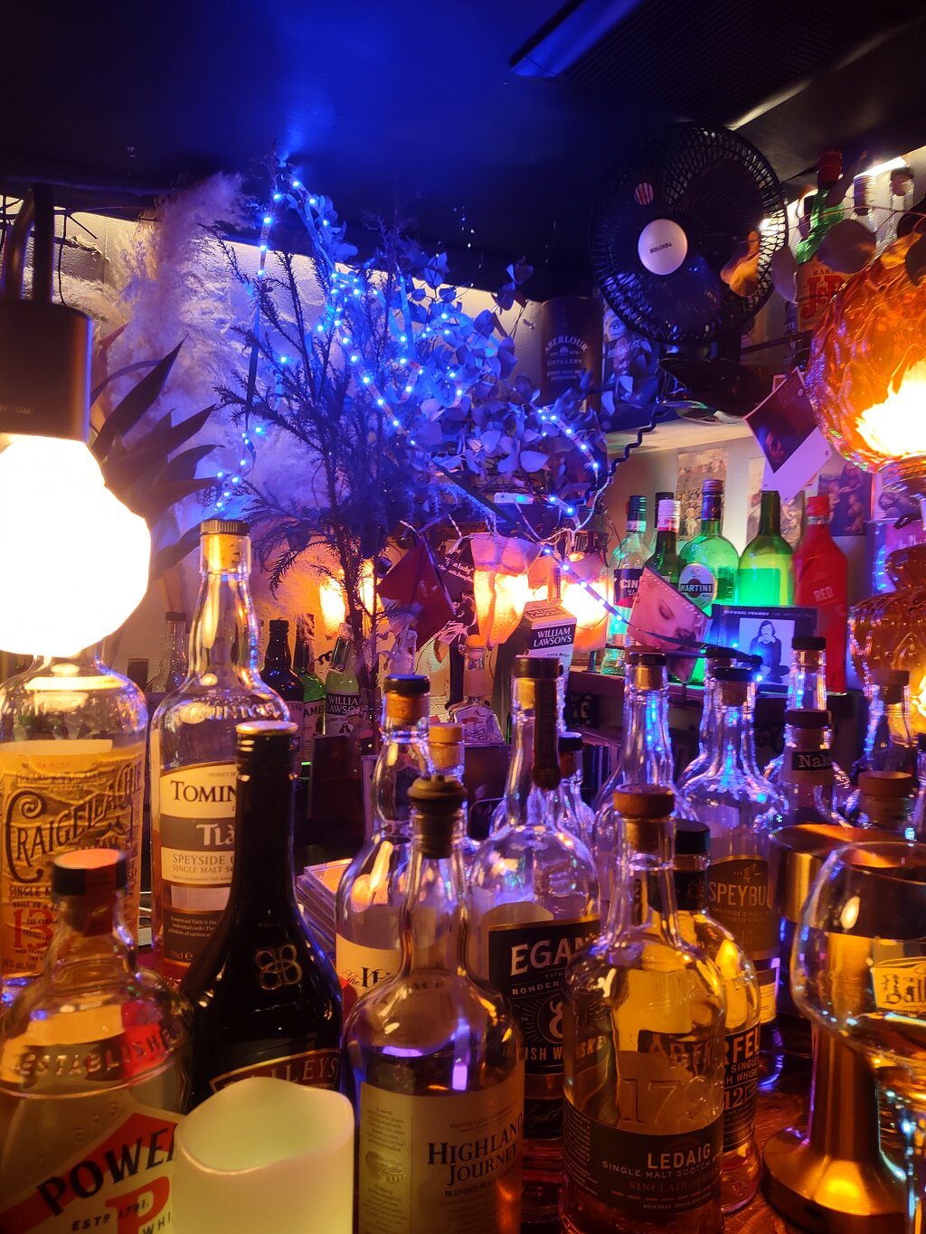 A whisky bar wall stacked with bottles under cool blue uplighting